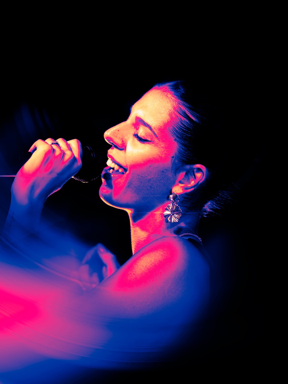 Una cantante sorride al microfono tra luce blu e magenta